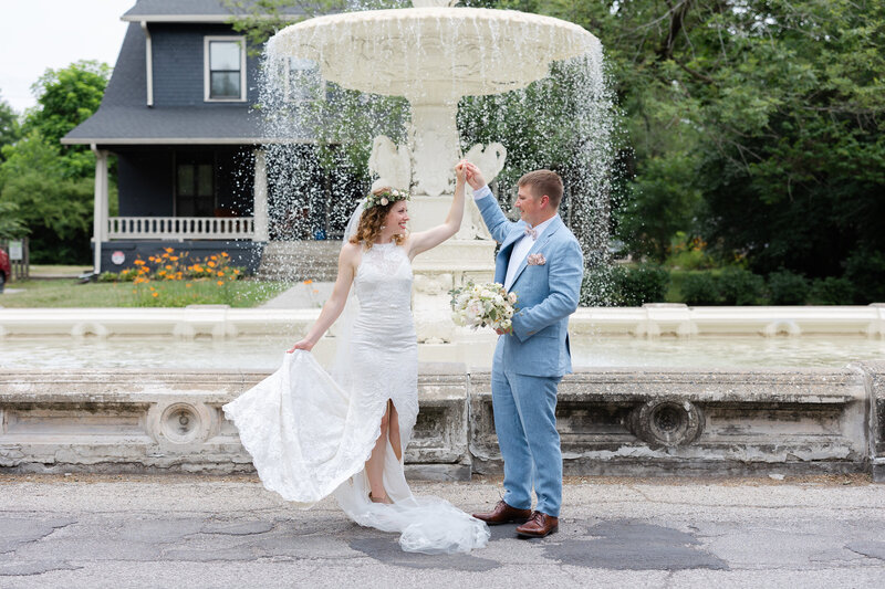 groom twirling bride in front of fountain