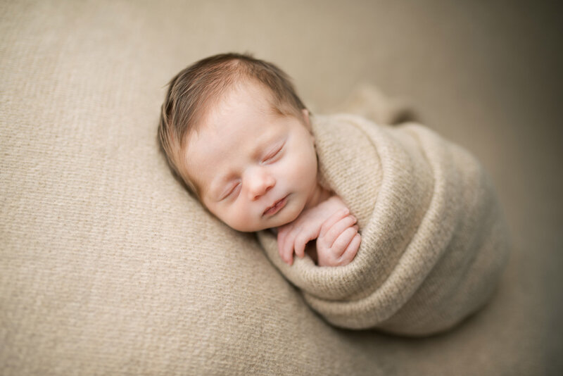 newborn with lots of hair wrapped in brown blanket