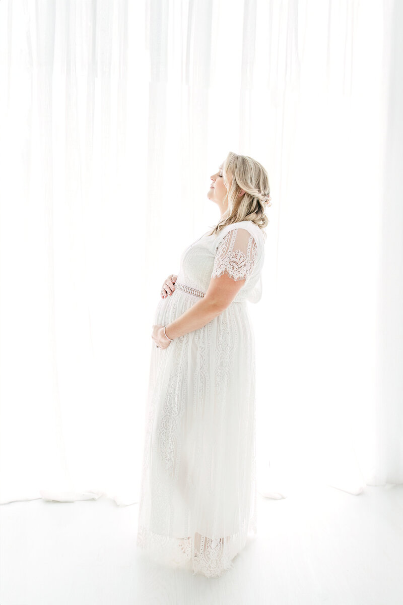 Pregnant woman looking down at belly in white dress