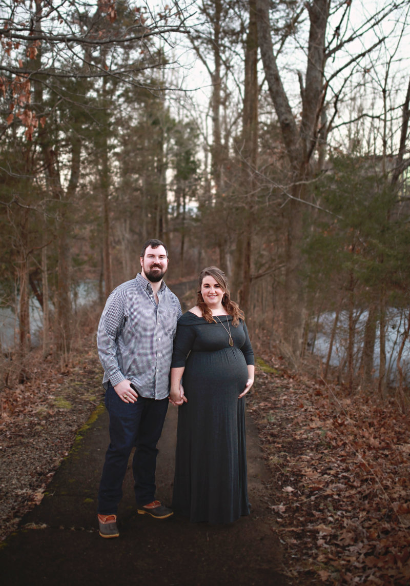 pregnant woman in long dark dress holding hands with man in fall outdoor scenery