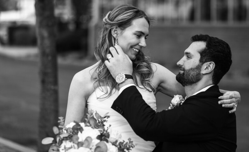bride and groom smile as groom caresses bride's cheek