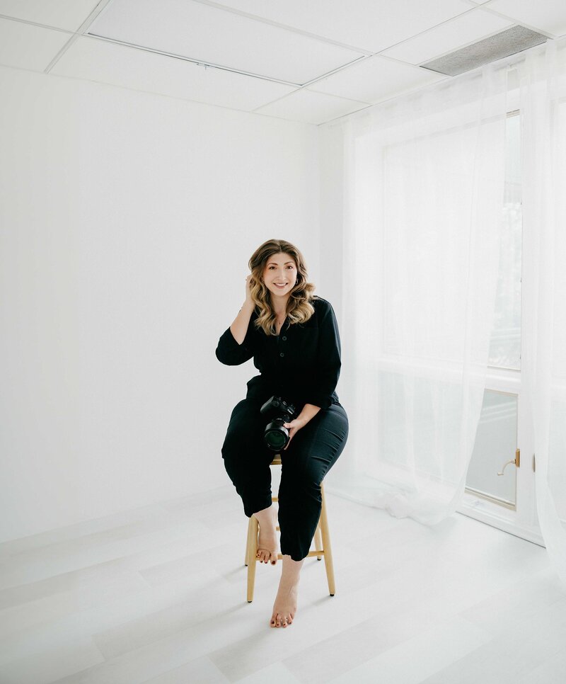 Photographer sits on barstool in photo studio with white backdrop