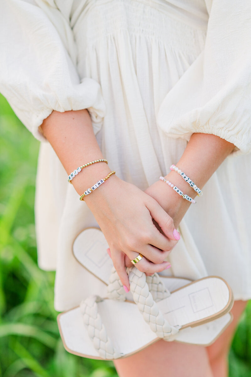 close up of a girl wearing bracelets and holding sandals