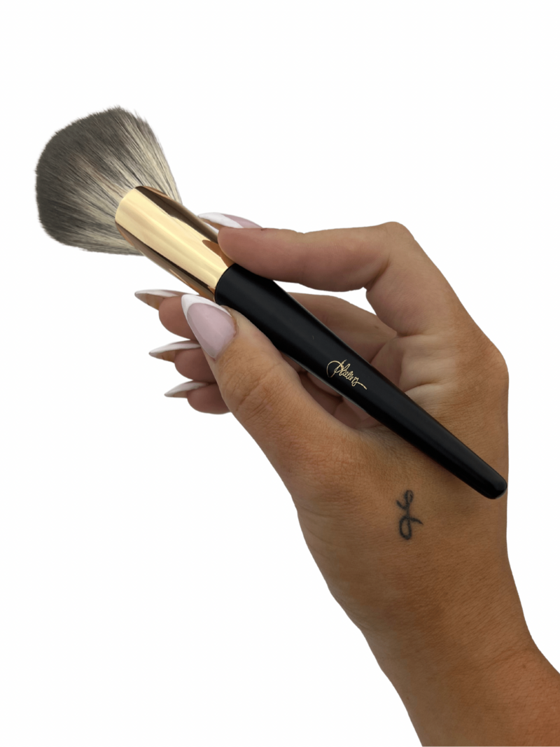 A hand holding a large makeup brush.