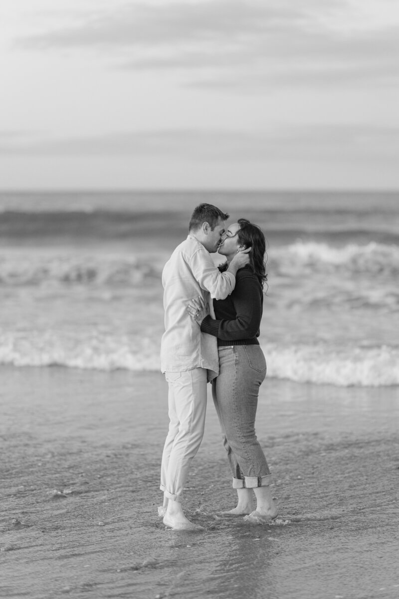 Engaged couple kissing in the water at sunset, capturing a candid moment of love.