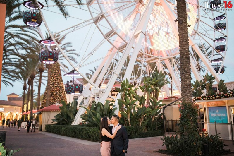 Engaged couple share a kiss in front of the Irvine Spectrum Ferris Wheel