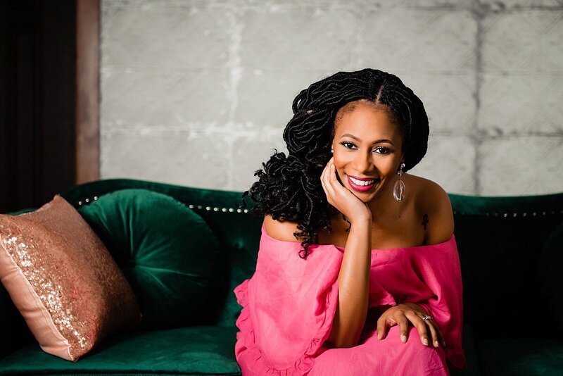 Elegant photo of Sheena Steward podcast host wearing a hot pink dress sitting on a green couch and smiling at the camera