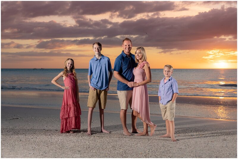 Family poses for a photo session on a Sarasota beach with a gorgeous sunset in the background.