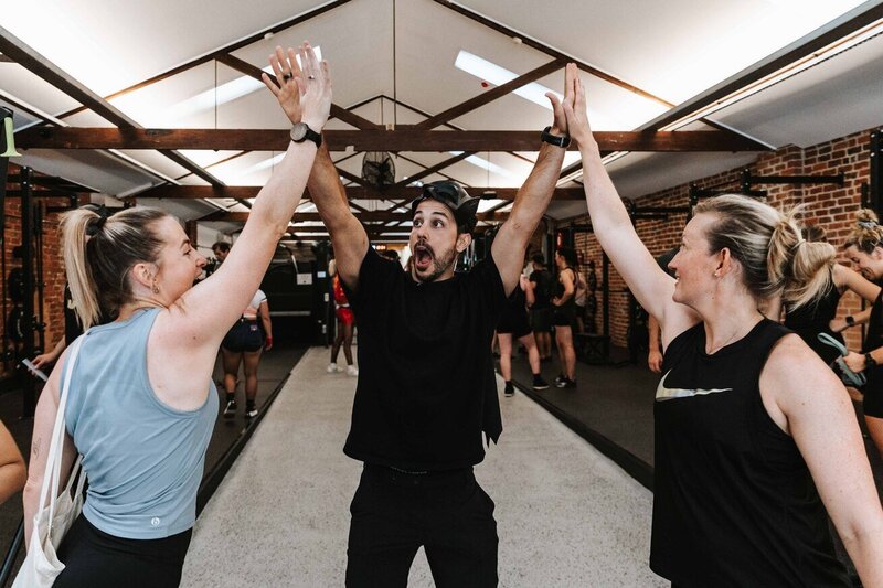 A group of gym-goers celebrating with high-fives in a bright and spacious Melbourne gym, capturing the community-focused and energetic vibe.