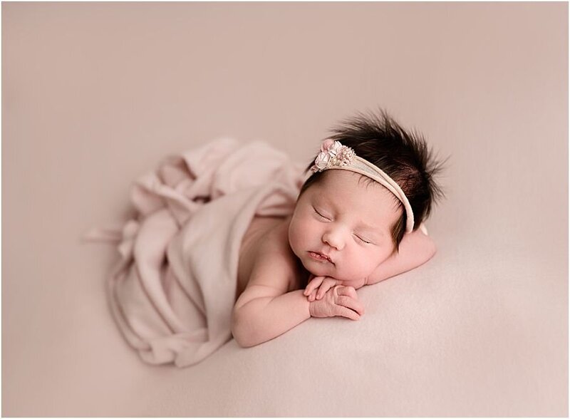 baby newborn girl, posed on chin on hands, on a pink backdrop