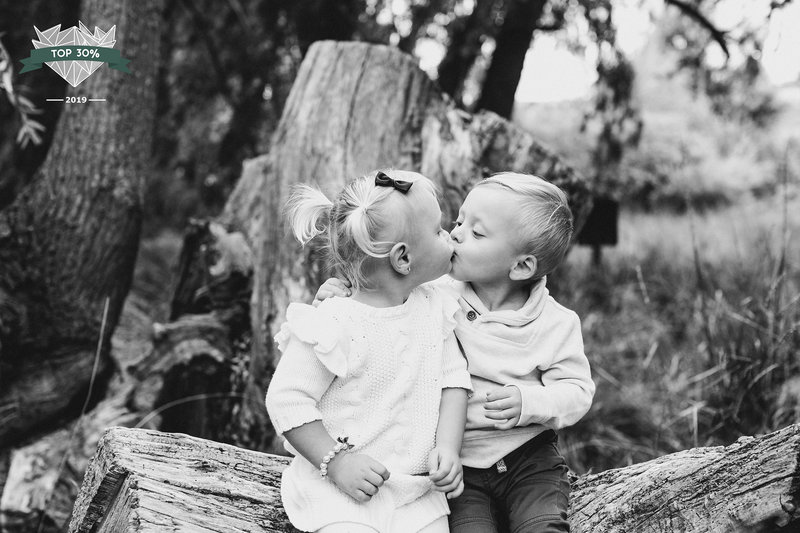 Twins kissing while sitting on a tree stump