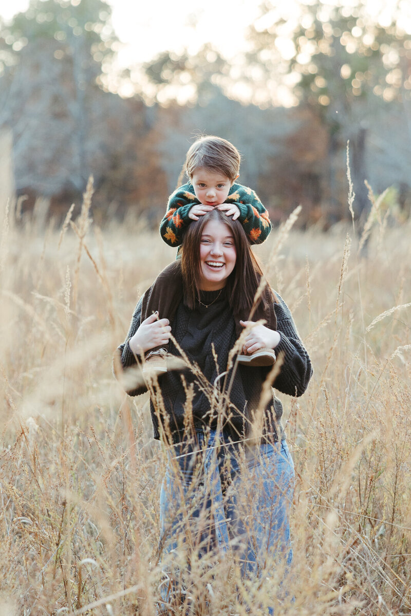 Toddler boy sitting on moms shoulders while they stand in a field of tall grass in the fall Farmington, Missouri. 