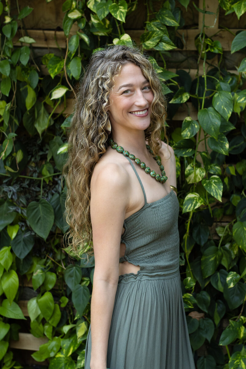 Dr. Mamie Burruss smiling and posing casually in front of a plant wall