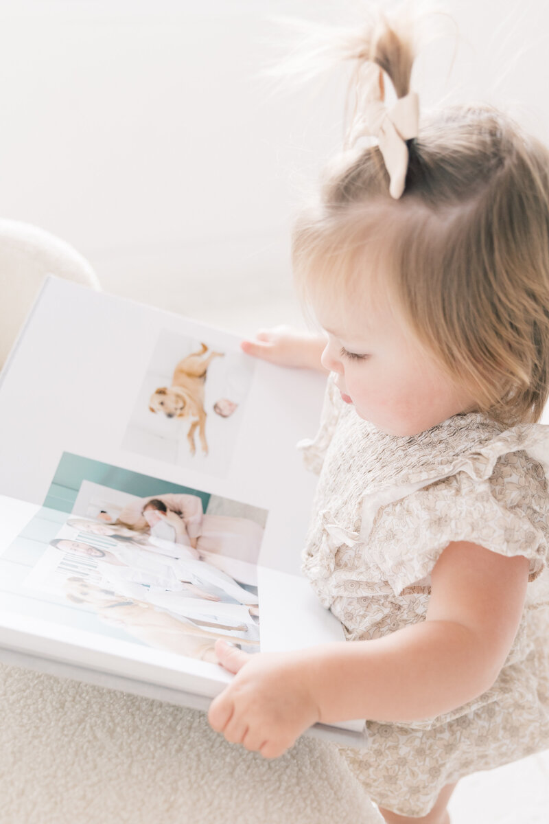 Young toddler reading a photo album, interacting with printed memories during a Charlotte family session.