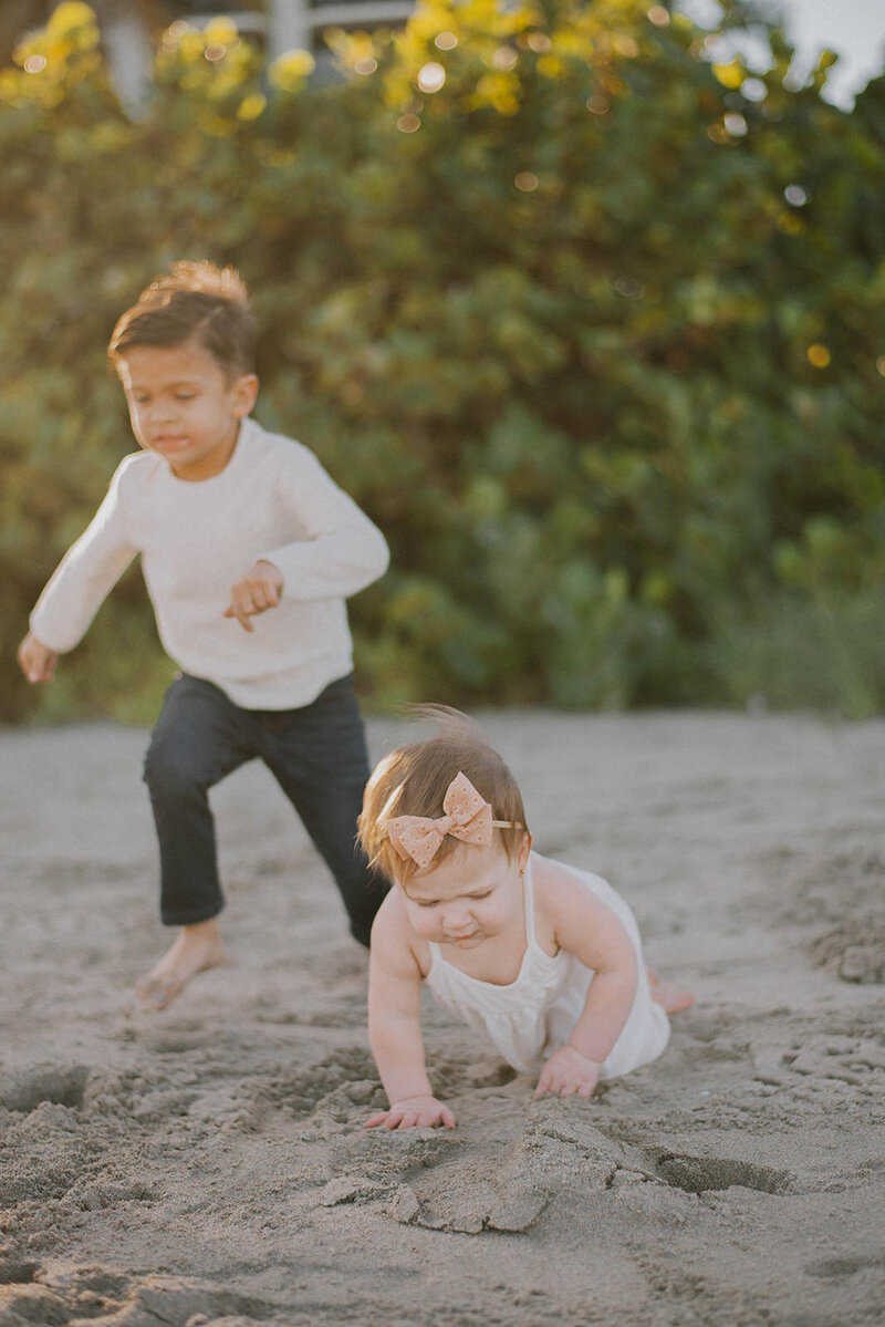 Toddler boy hugs his baby sister on the beach and smiles