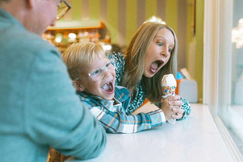 A mom playfully pretending she is going to eat all of her son's ice cream cone.
