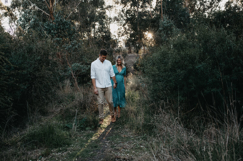 couple maternity session walking through nature at golden hour