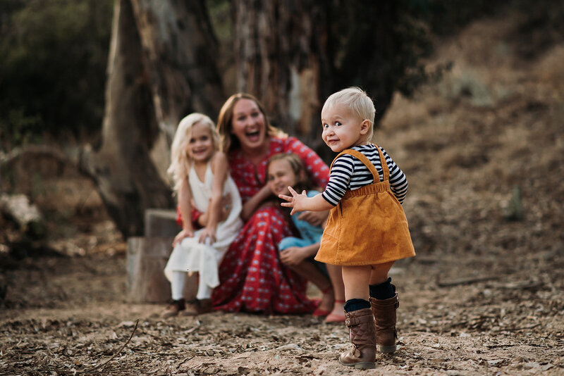 Toddler peeks back at camera while running toward mom and sisters in family photo