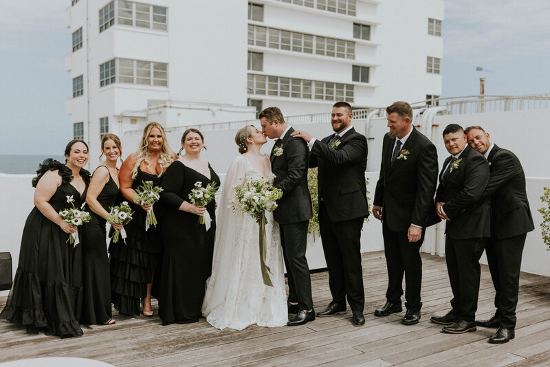 Bride and Groom kiss surrounded by their wedding party.