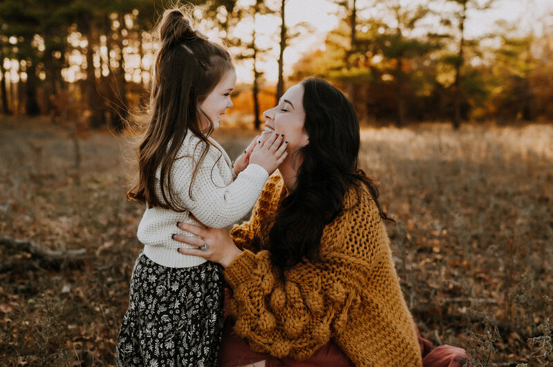 A daughter holding her mom's cheeks and smiling in the pine trees of Alvord, Texas