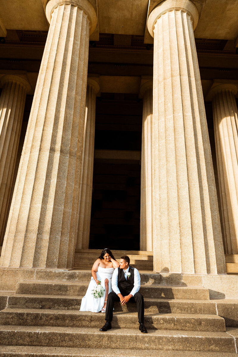 Couple sitting on the Nashville Parthenon stairs in dramatic pose wearing wedding outfits