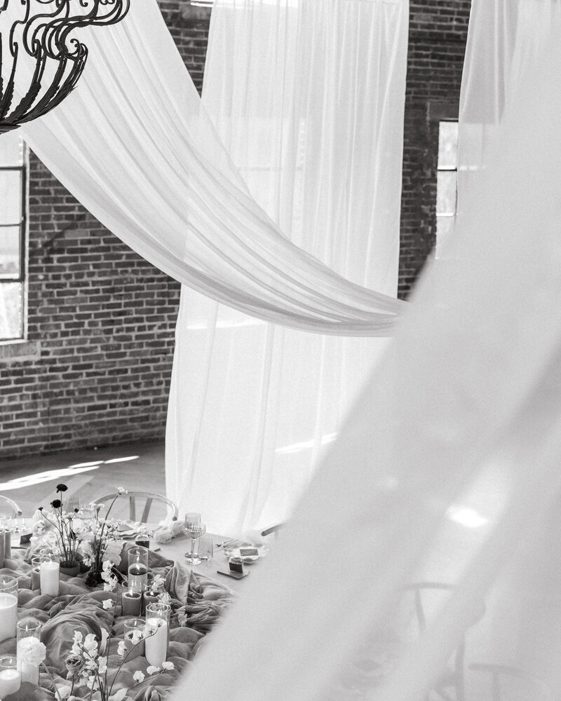 Romantic wedding tablescape framed by flowing sheer drapes in an industrial loft with brick walls