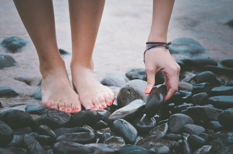 barefoot woman on a beach picking up rocks