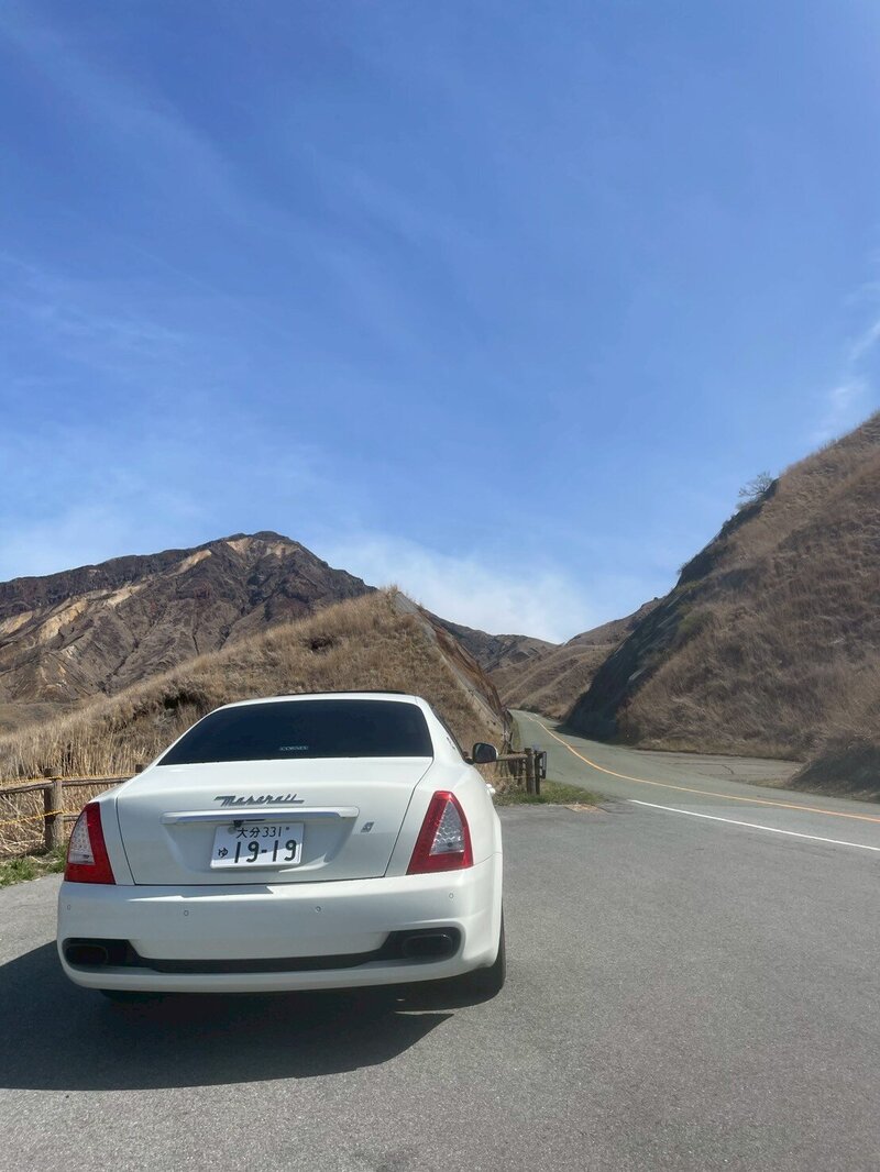 Rear view of a white Maserati driving along an open mountain road under a clear blue sky, evoking a sense of freedom and adventure.