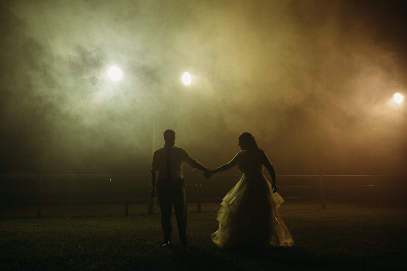 Silhouetted couple holding hands under bright lights on a foggy night