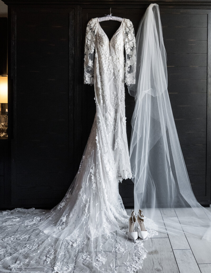 Close-up of a wedding dress, shoes, and veil elegantly arranged against a dark background, showcasing intricate details and texture.