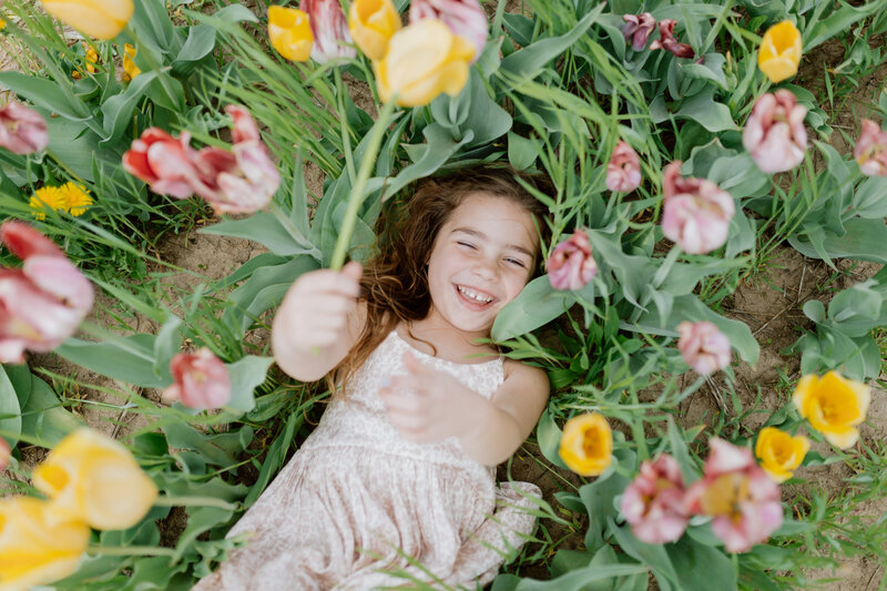 A young girl holds a yellow tulip while laying amongst white and pink tulip fields at the Midwest Tulip Festival in Illinois.