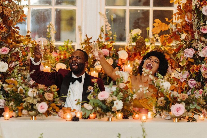 Lush growing florals surround the couple at this autumnal wedding’s sweetheart table composed of roses, ranunculus, lisianthus, dried hydrangea, delphinium, copper beech, and fall foliage creating hues of dusty rose, burgundy, mauve, copper, terra cotta, and hints of lavender. Design by Rosemary and Finch in Nashville, TN.