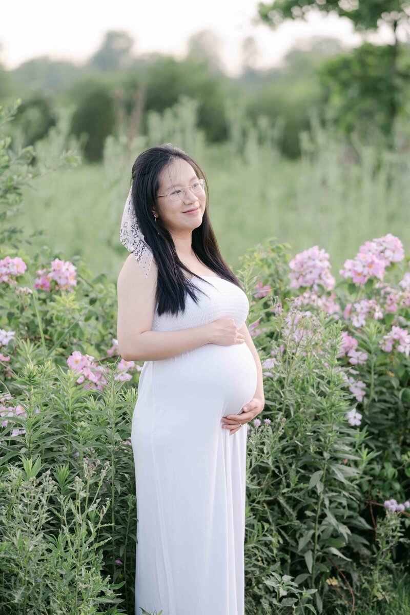 a mom to be poses in a white dress as she smiles at her husband