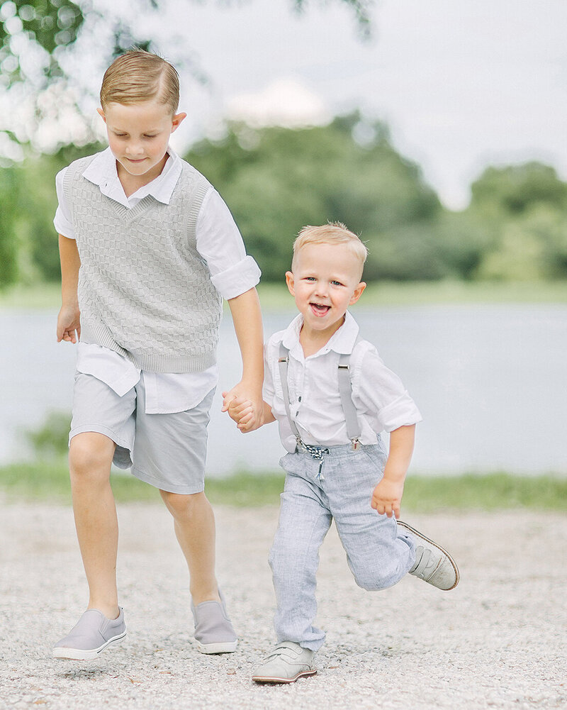 Two young brothers holding hands and running in front of a lake