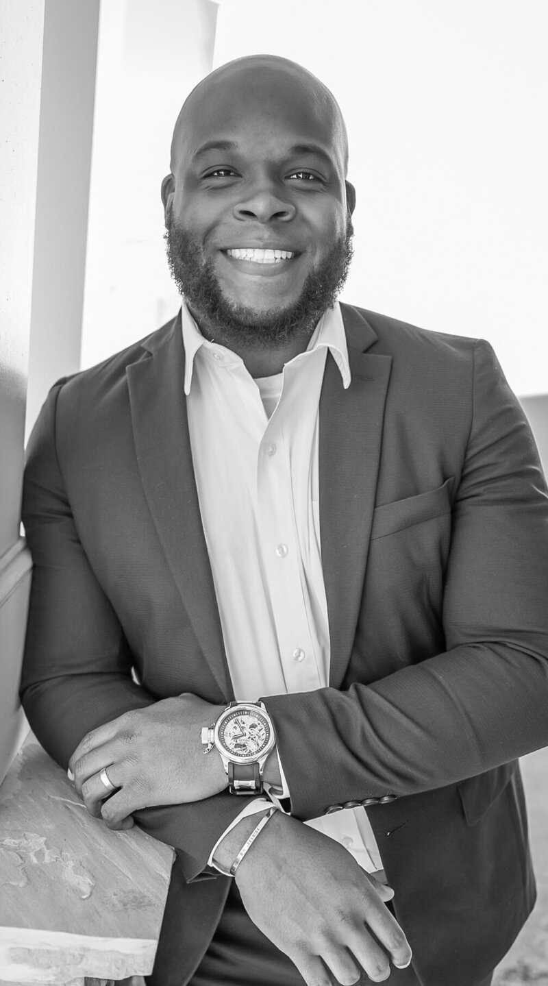 a black and white photo of a man dressed in business attire smiling at the camera. photographed by Millz Photography in Greenville, SC