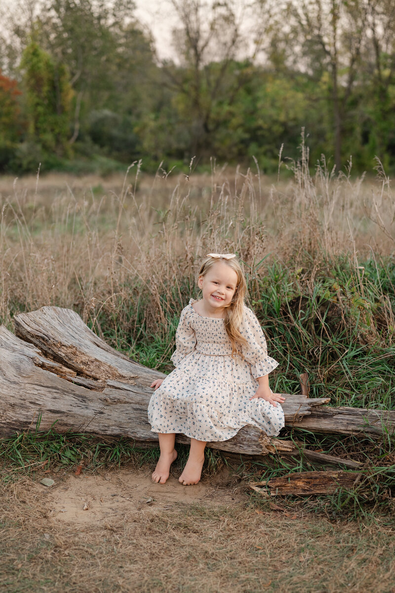 Joyful girl sitting on a log in a sedge meadow, surrounded by soft grass.