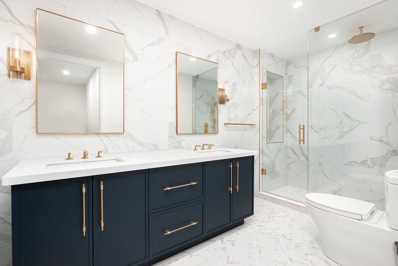 Bathroom design with full marble slab walls and shower tile, gold hardware, and navy blue cabinets.
