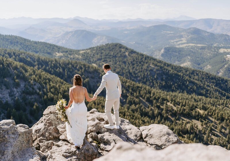 Couple holding hands on a rocky cliff during their Boulder Colorado elopement at Lost Gulch Overlook, captured by a Colorado elopement videographer Alpine Vows.