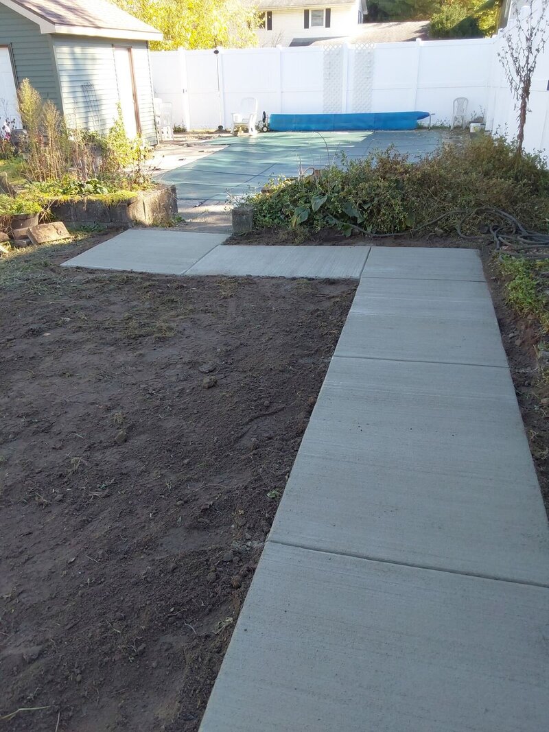 New concrete walkway with tooled control joints leading back toward a backyard pool in Osceola, IN