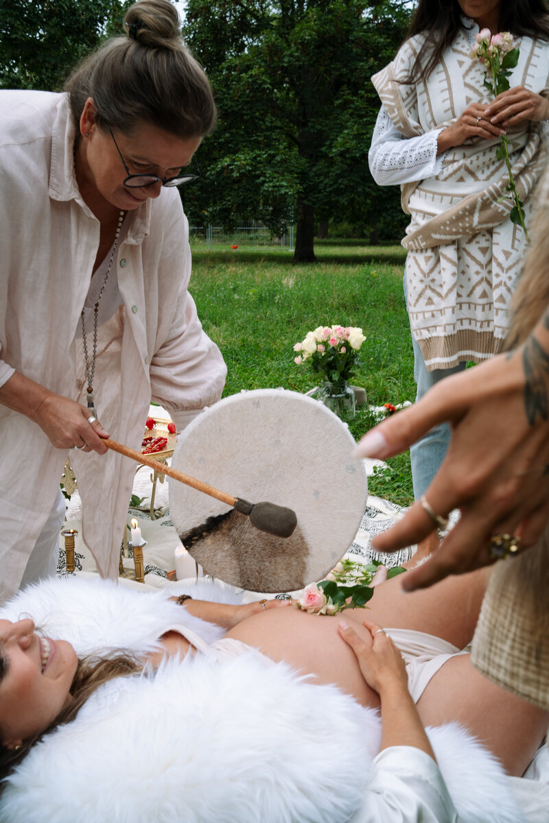 Pregnant woman smiling, circle of women drumming ritual