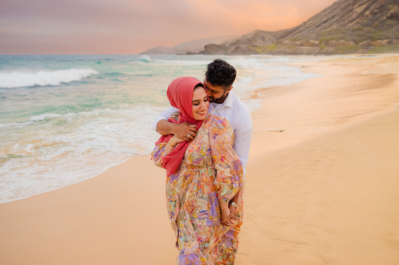 oahu engagement session woman wearing a long beautiful dress and husband kissing her cheek