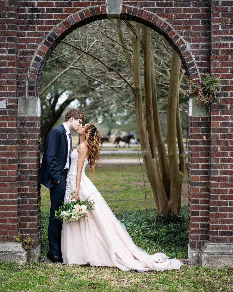 Bride and groom kissing in brick archway in New Orleans Audubon Park
