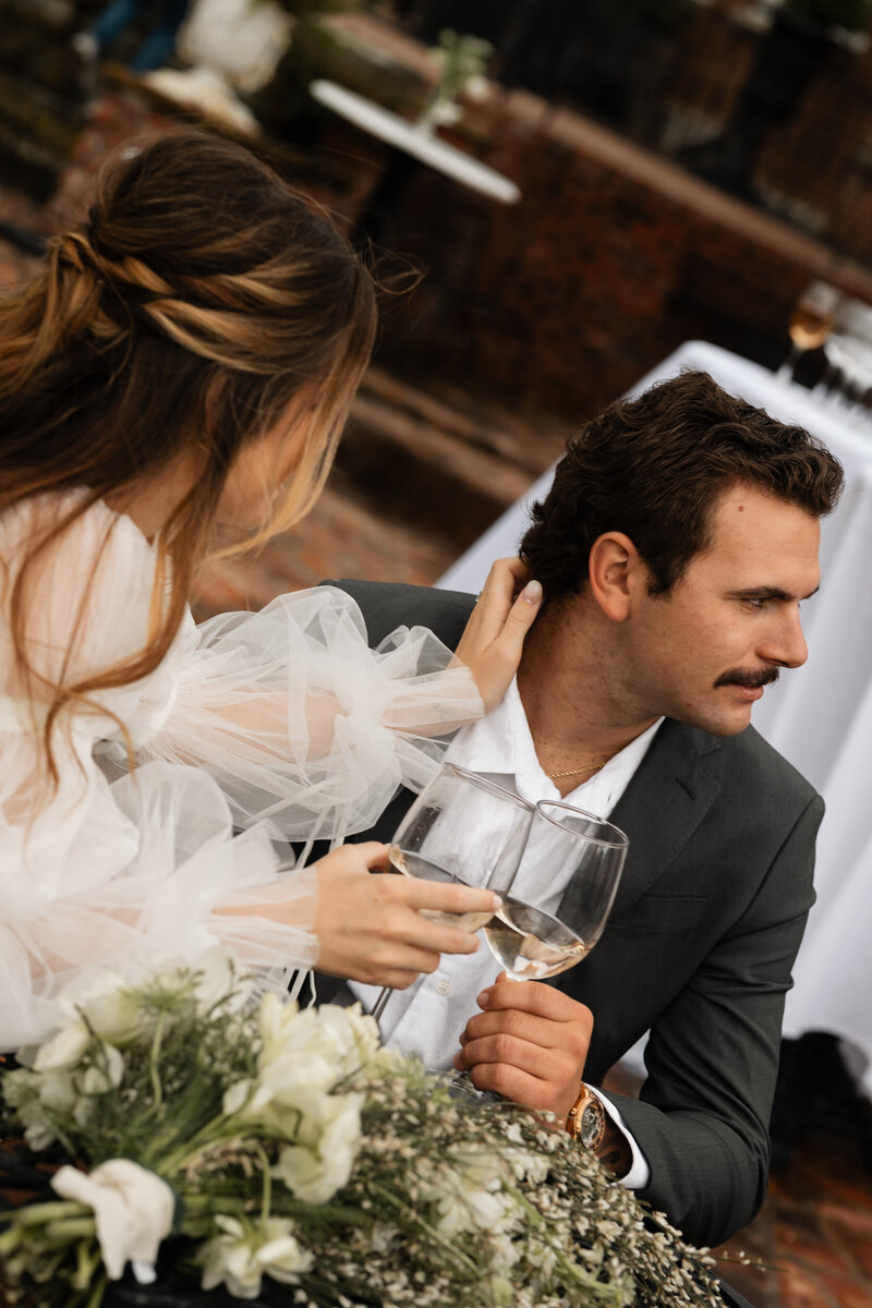 Wedding couple holding champagne glasses while listening to toasts during their reception, captured in a candid and heartfelt moment of celebration.