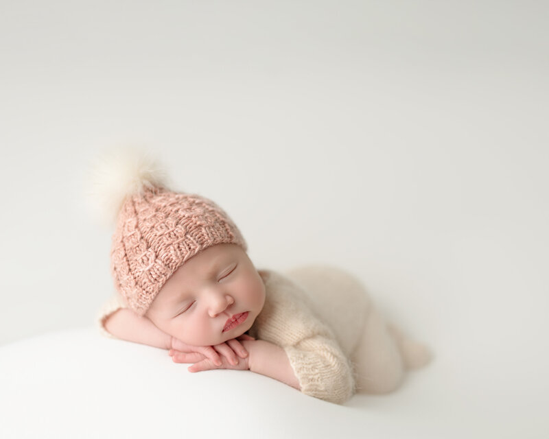 Newborn girl wearing pink knit hat and posed on white backdrop – timeless and cozy newborn image from Paris, Ontario.