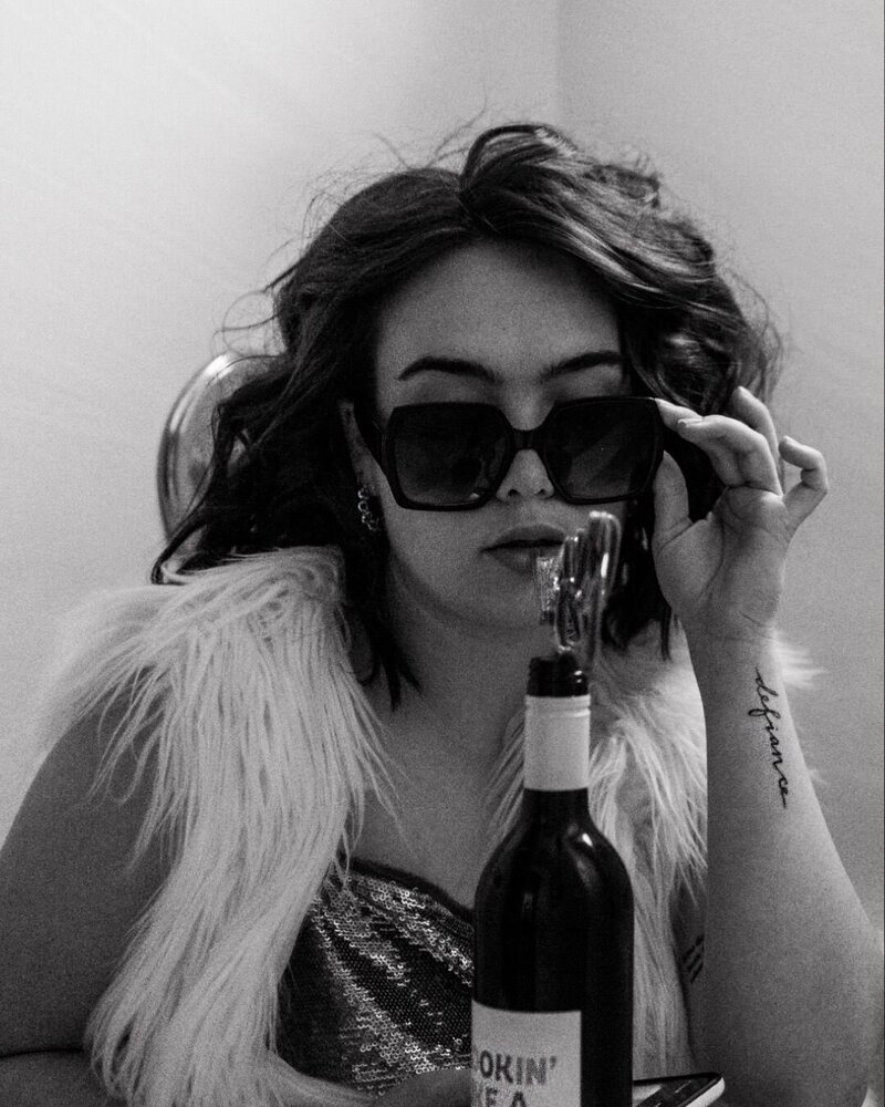 black and white image woman with sunglasses and wine bottle