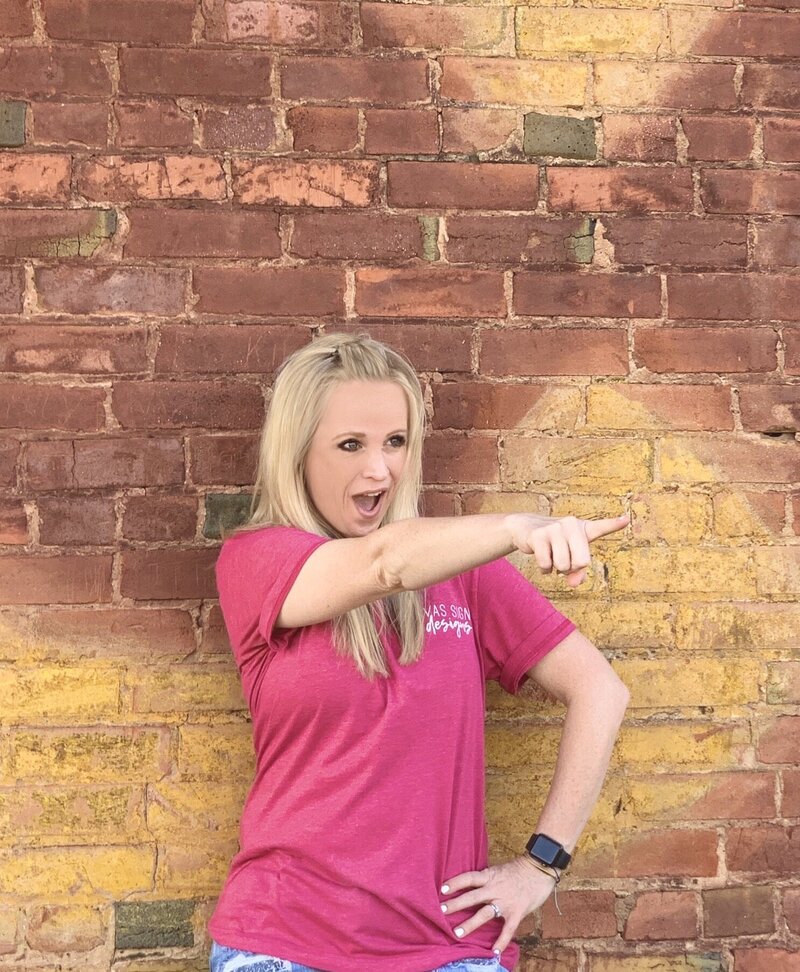 Blonde woman in pink shirt pointing on red and yellow brick background