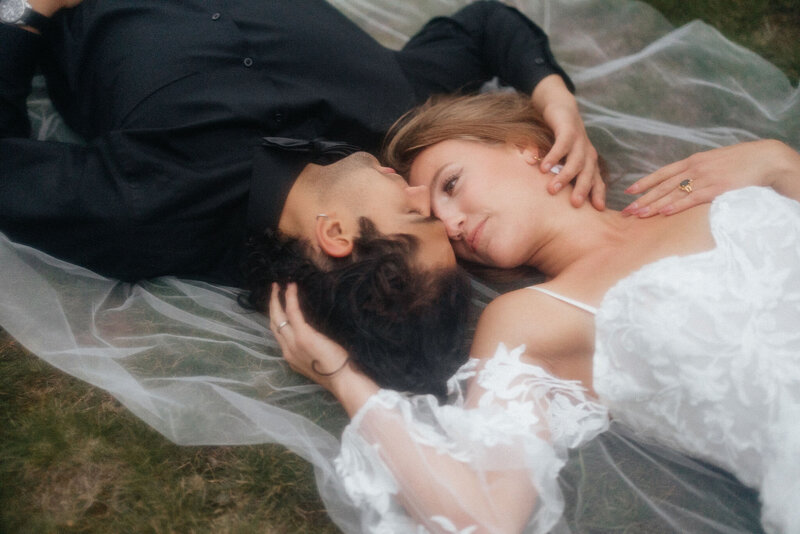 bride and groom laying on the grass faces towards one another