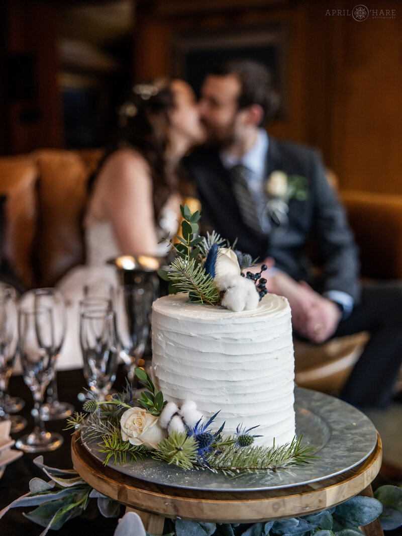 Couple Kiss with their White Wedding Cake in the foreground at Romantic Riversong Inn Estes Park CO
