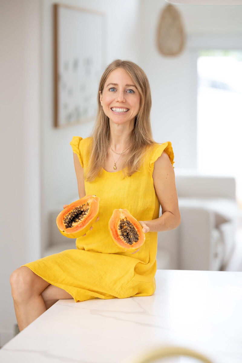 Olivia Budgen sitting on a kitchen bench holding a cut papaya