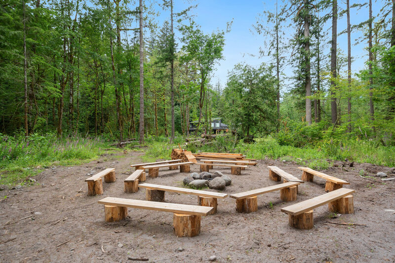 Outdoor fire pit surrounded by wooden benches in a forest clearing